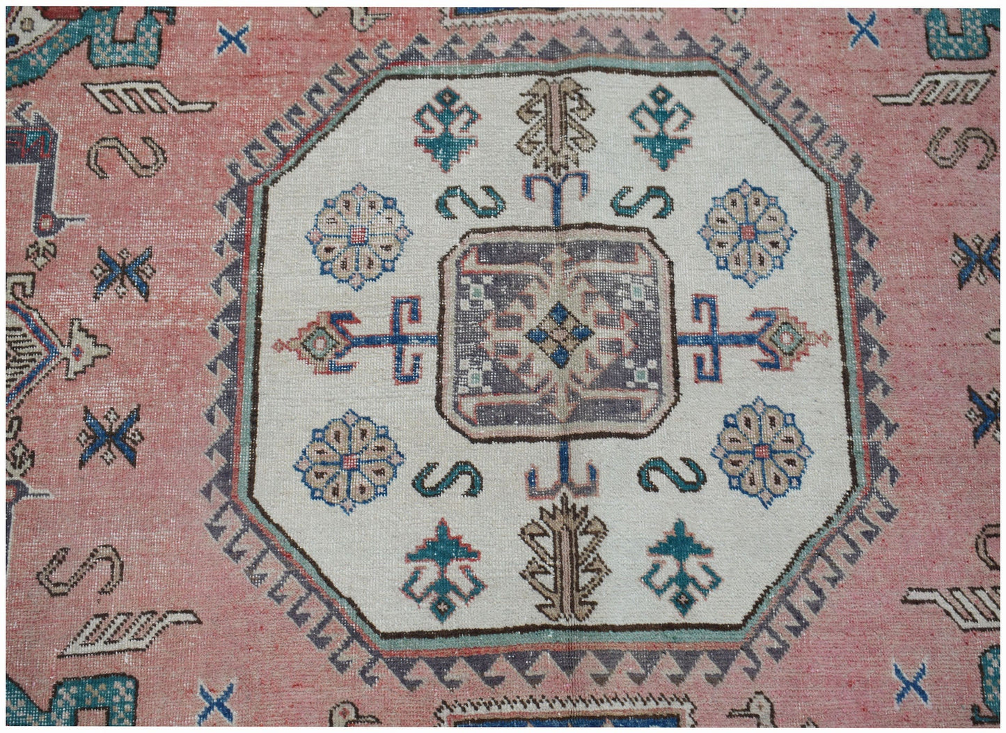 A vintage handmade Caucasian wool rug featuring a central medallion on a pink field.