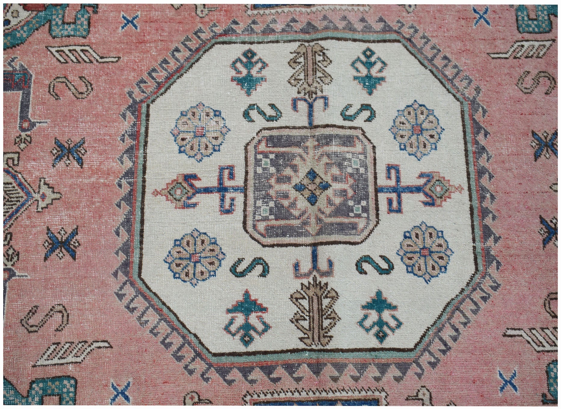 A vintage handmade Caucasian wool rug featuring a central medallion on a pink field.