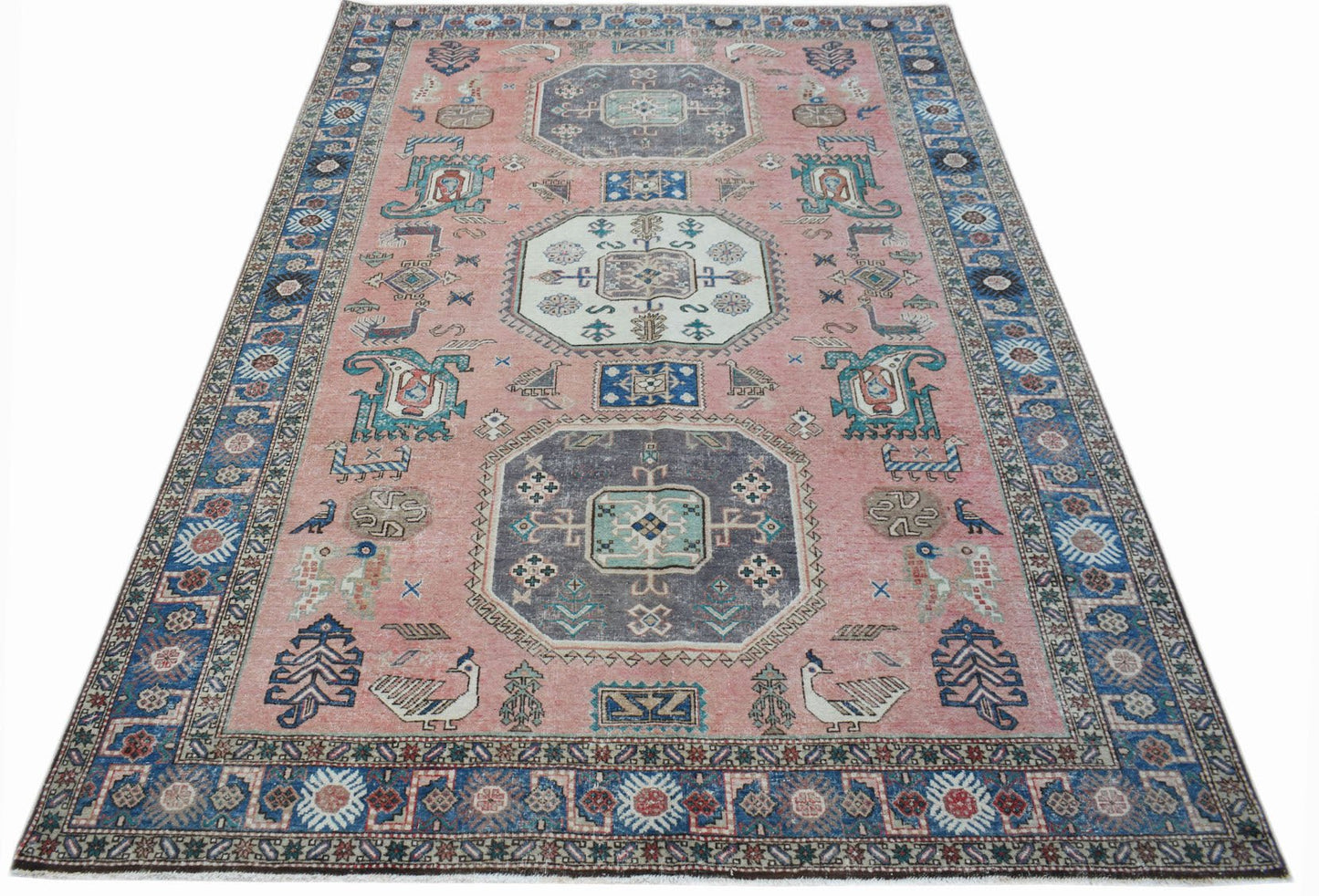 A vintage handmade wool rug from the Caucasus featuring a pink field with traditional motifs.