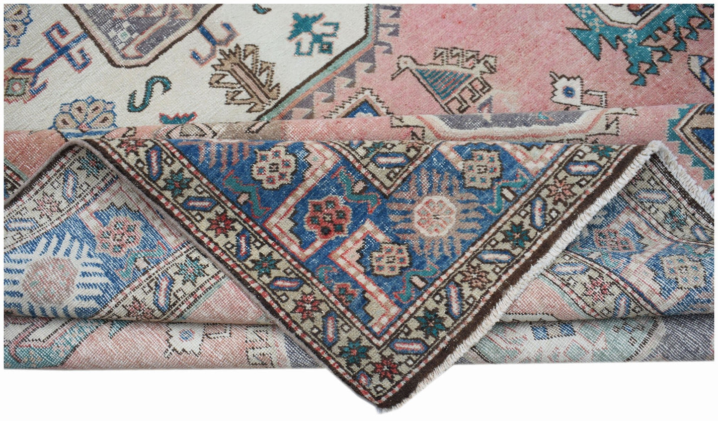 A vintage handmade Caucasian wool rug featuring a traditional geometric pattern in pink and blue.