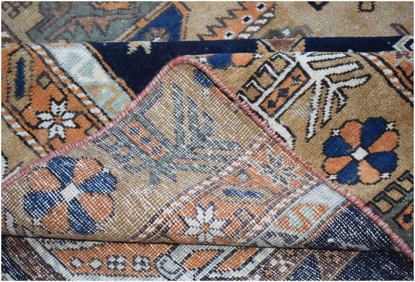 A handwoven vintage Persian rug featuring geometric floral patterns in blue, orange, and tan.