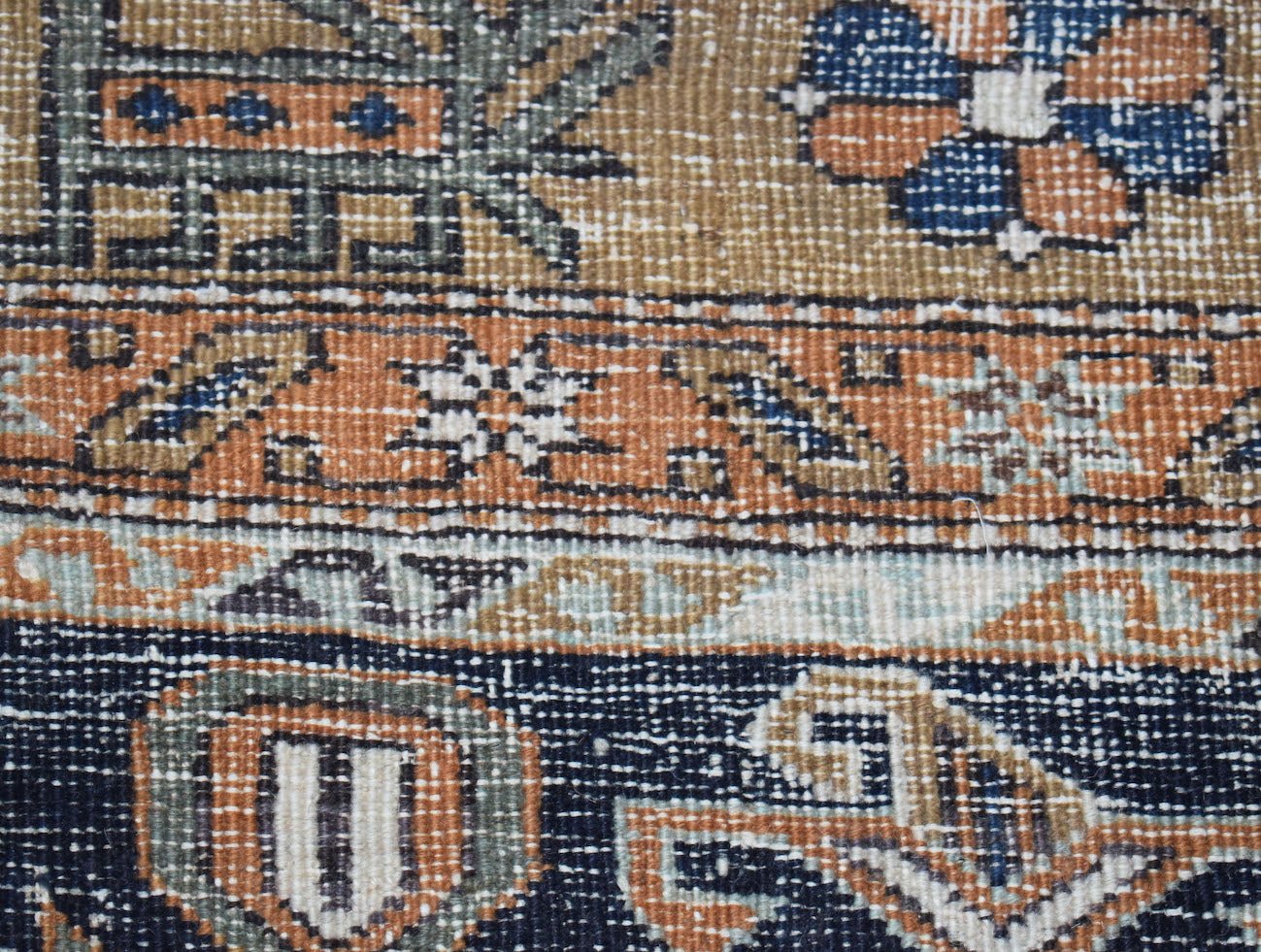 A close-up of a vintage handwoven Persian rug featuring geometric patterns in blue and orange.