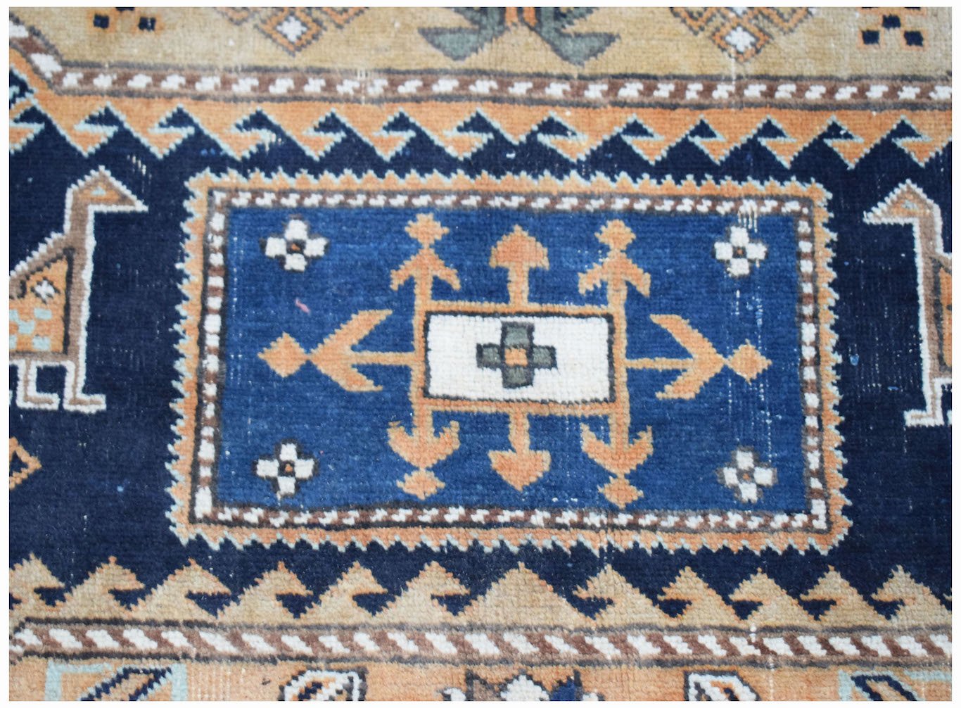 A vintage handwoven Caucasian rug featuring a central blue medallion with geometric motifs.