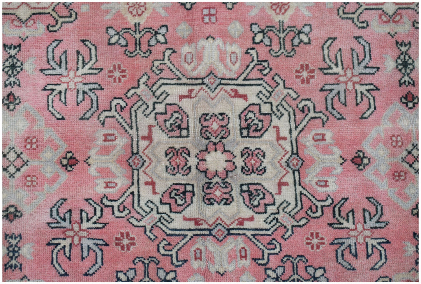 A vintage handwoven Chinese rug featuring a central floral medallion on a faded pink background.