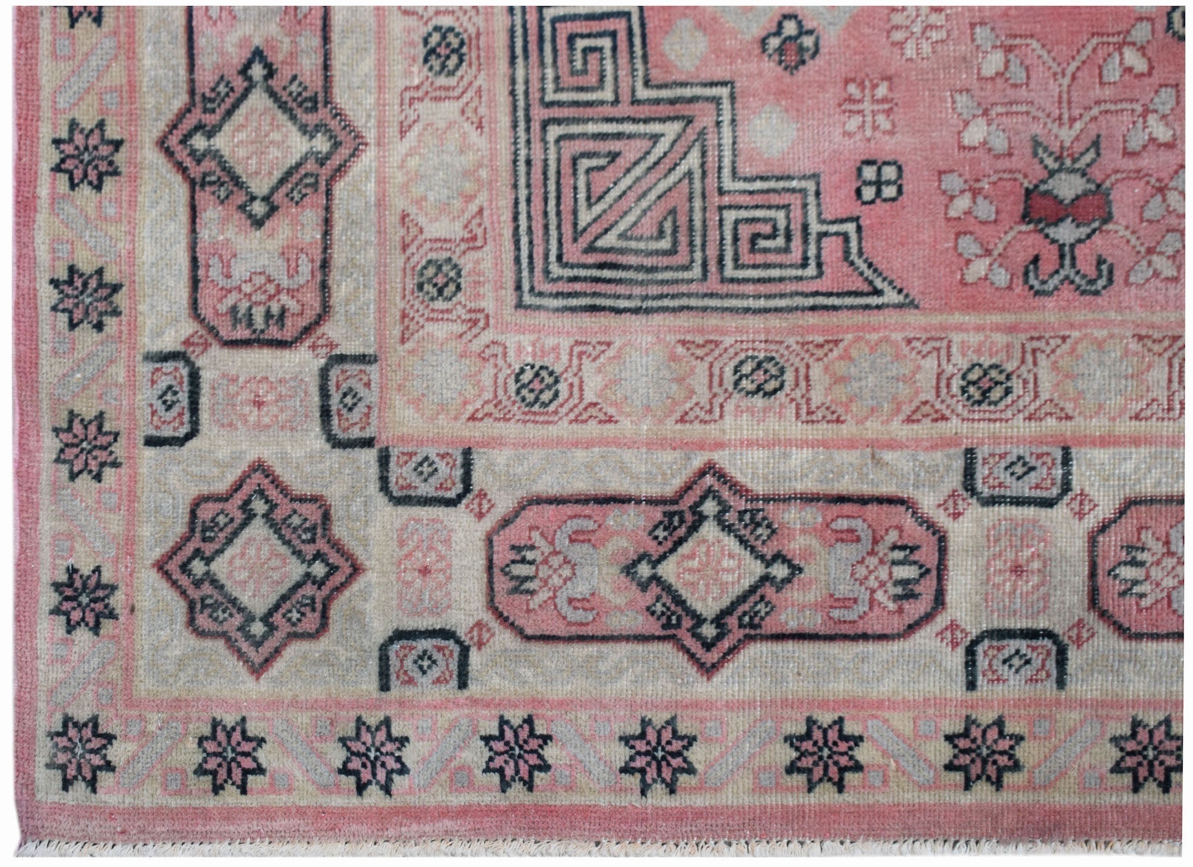 A vintage handwoven Chinese rug featuring geometric patterns in shades of pink and grey.