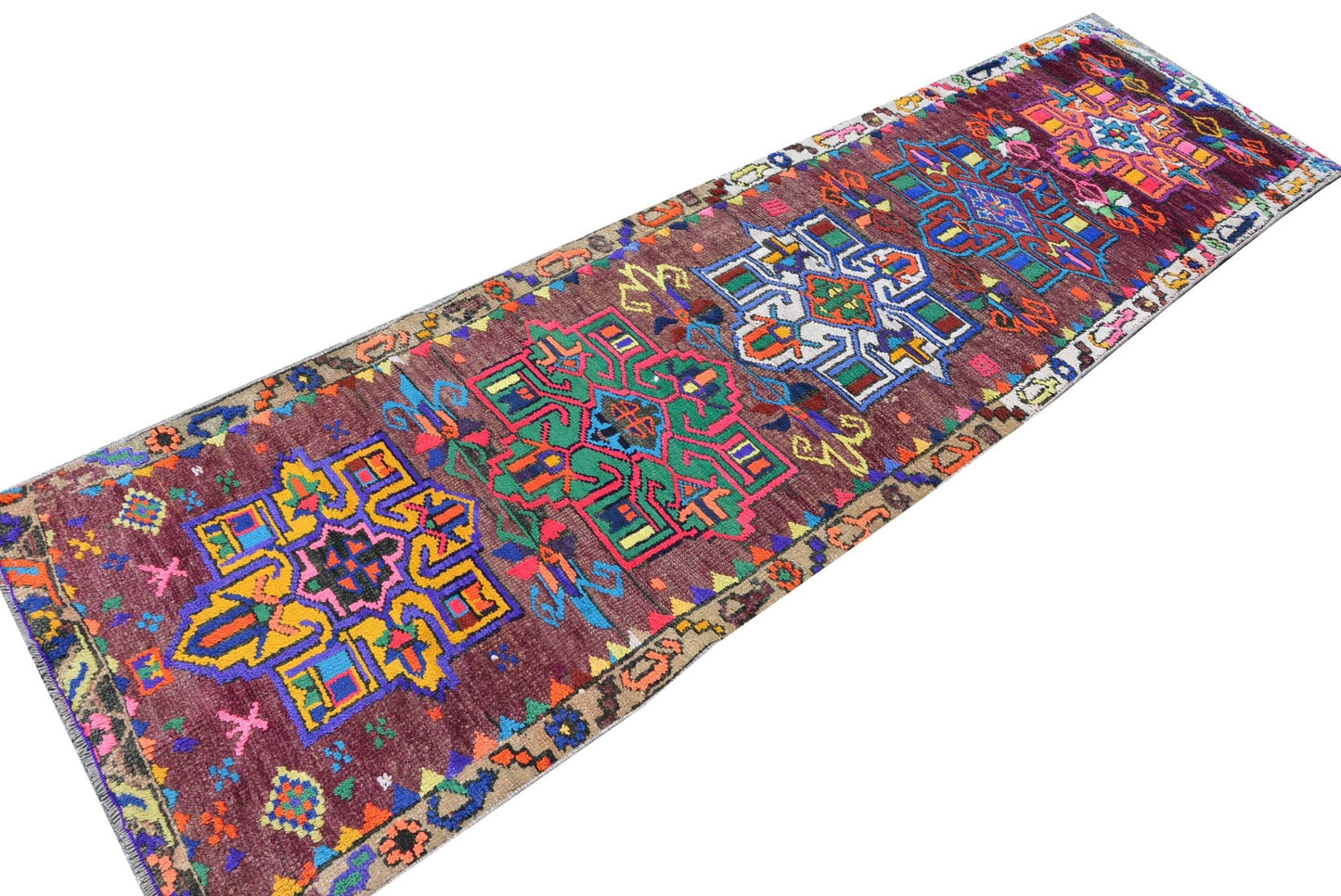 A vintage Kurdish Herki runner featuring vibrant tribal motifs on a deep purple wool background.