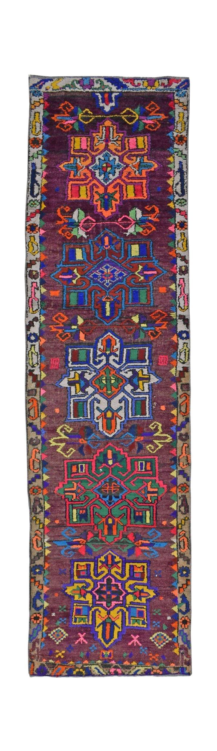 A vintage Kurdish Herki runner featuring vibrant tribal motifs on a deep purple wool background.
