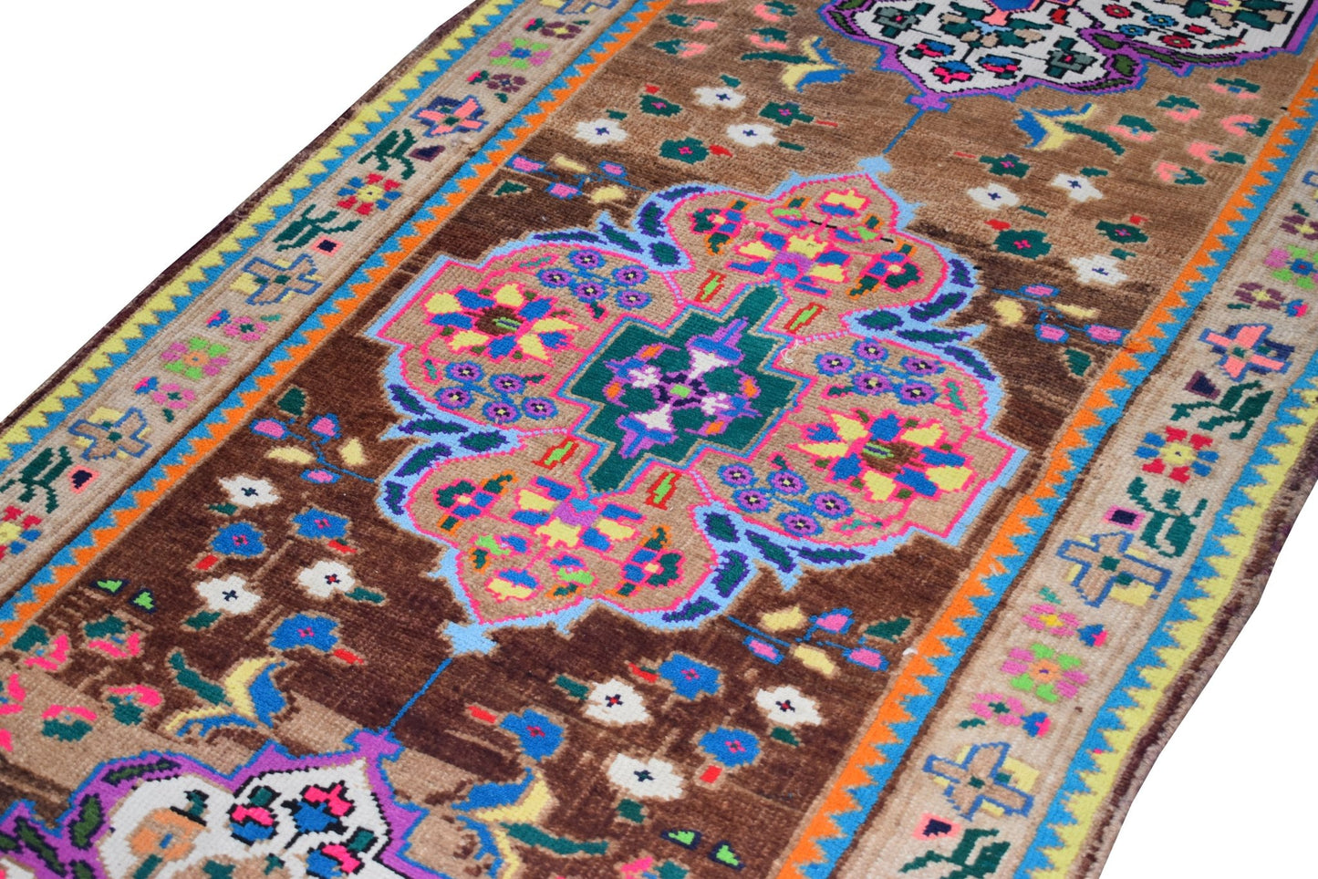 A vintage Kurdish Herki runner featuring a brown field with colorful tribal floral motifs.