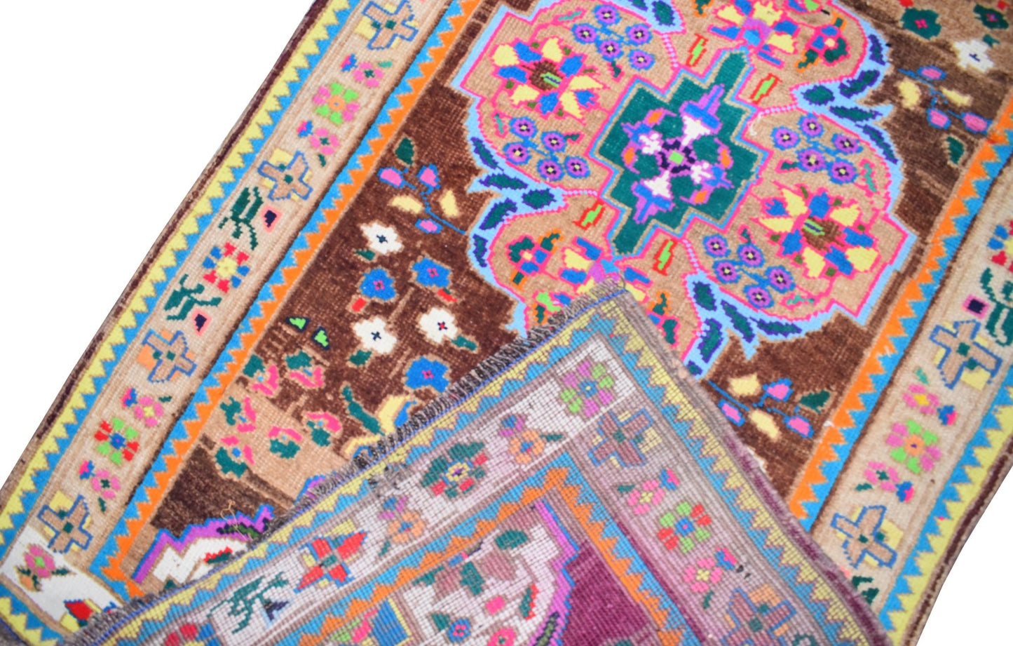 A vintage Kurdish Herki runner featuring vibrant tribal motifs and geometric patterns on a brown field.