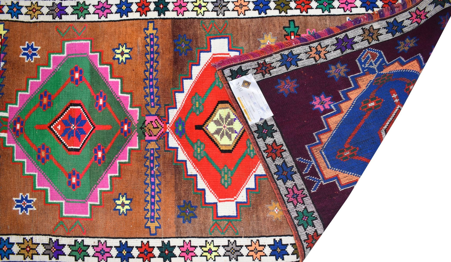 A vintage Kurdish Herki runner featuring geometric tribal motifs in vibrant colors on a brown field.