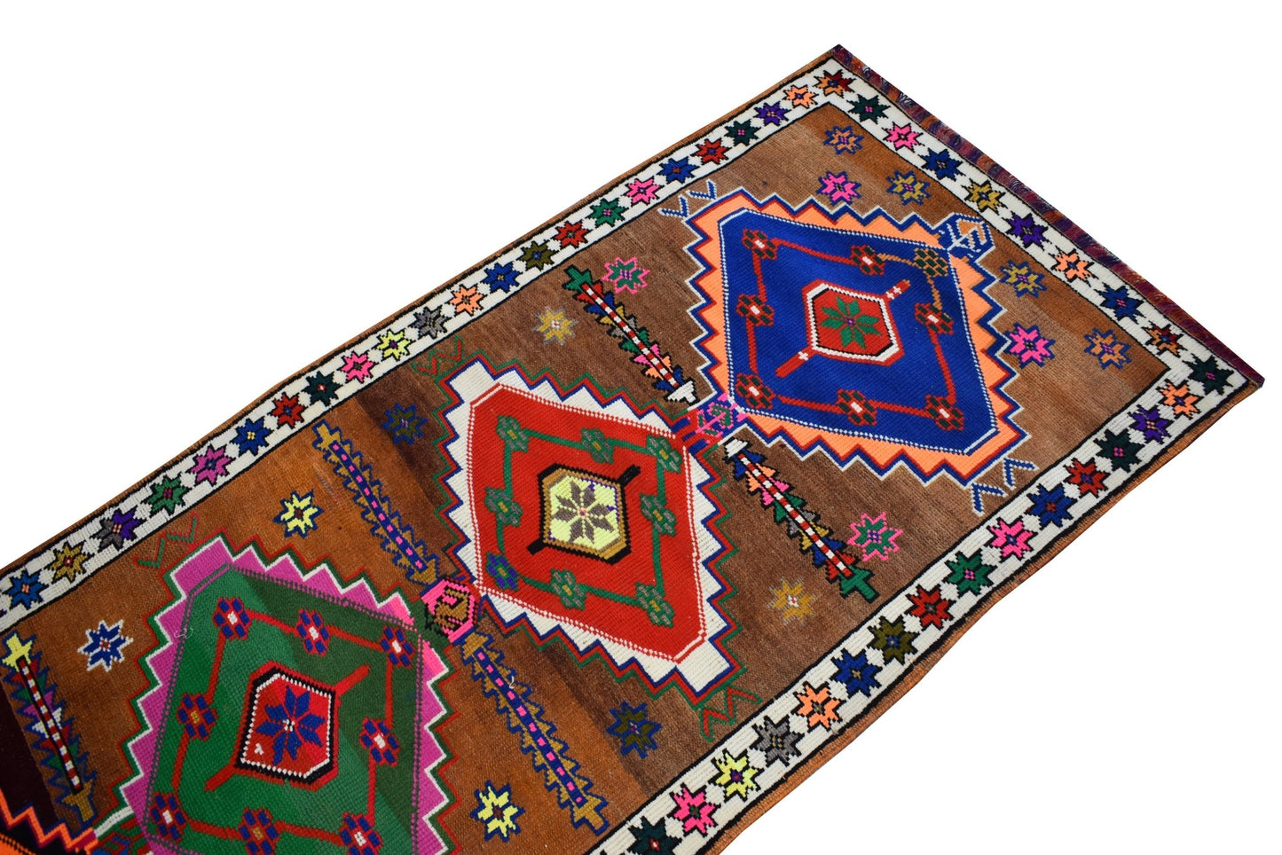 A vintage Kurdish Herki runner featuring colorful tribal geometric motifs on a brown wool field.