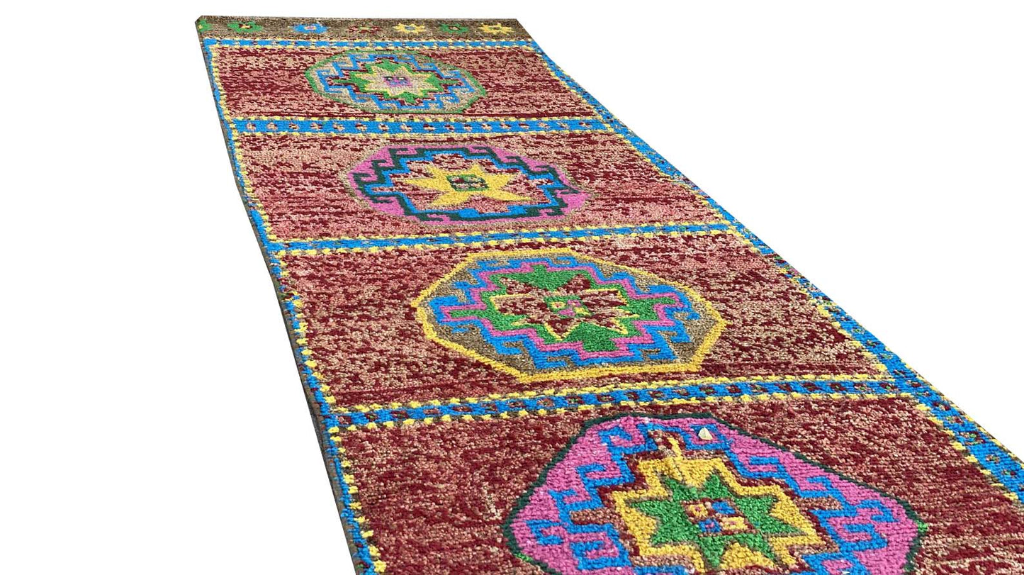 A vintage handmade Kurdish Herki runner featuring colorful geometric medallions on a red field.