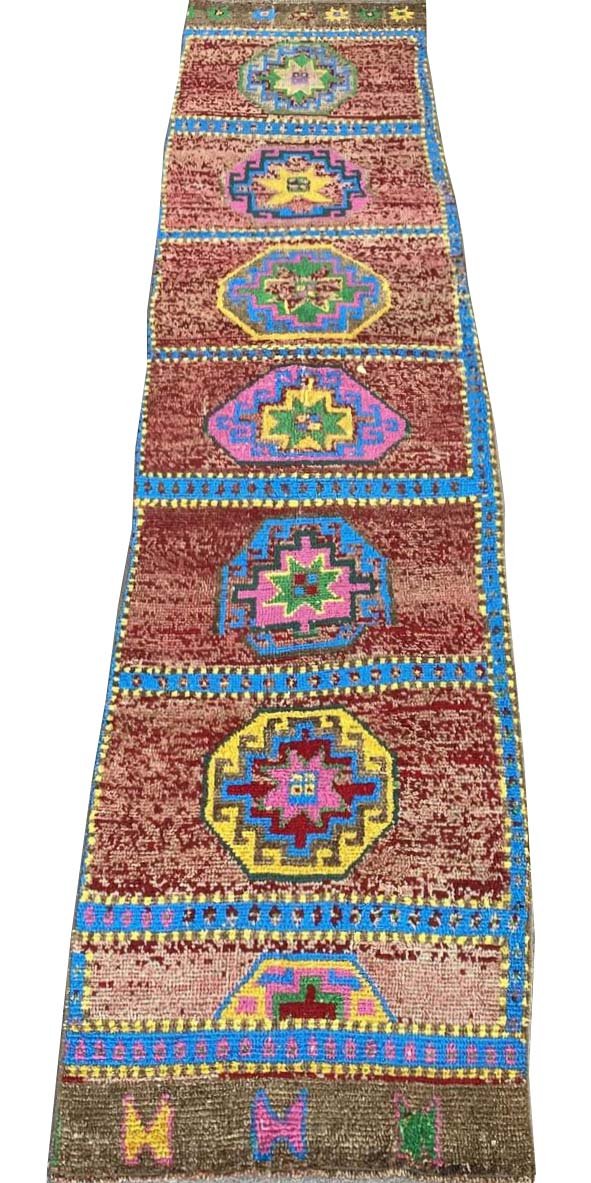 A vintage handmade Kurdish Herki runner featuring geometric medallions on a red wool background.