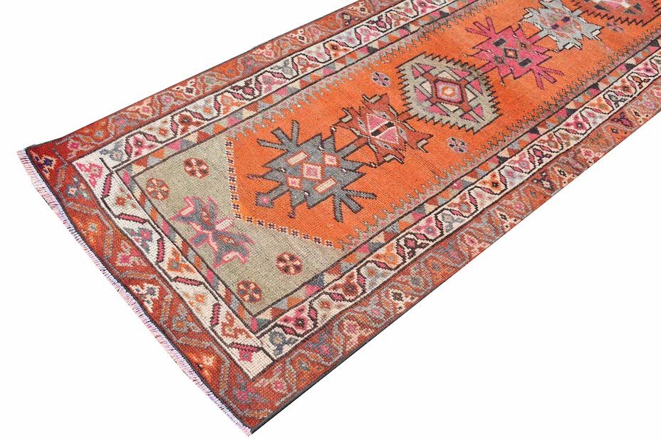 A vintage Kurdish Herki runner featuring tribal motifs in vibrant orange and neon colors.