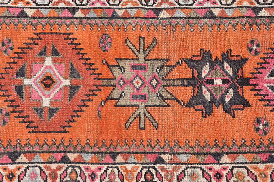 A vintage Kurdish Herki runner featuring tribal geometric motifs in vibrant orange and pink tones.