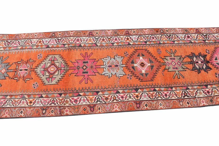 A vintage Kurdish Herki runner featuring tribal geometric motifs in vibrant orange and neon tones.