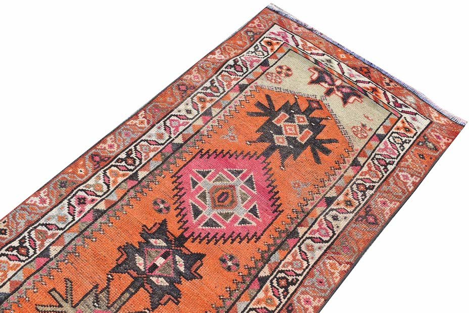 A vintage Kurdish Herki runner featuring tribal motifs in vibrant orange and pink wool.