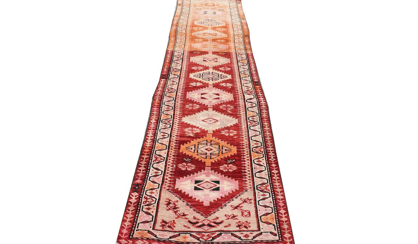 A vintage Kurdish Herki runner featuring tribal motifs in vibrant red, orange, and pink tones.