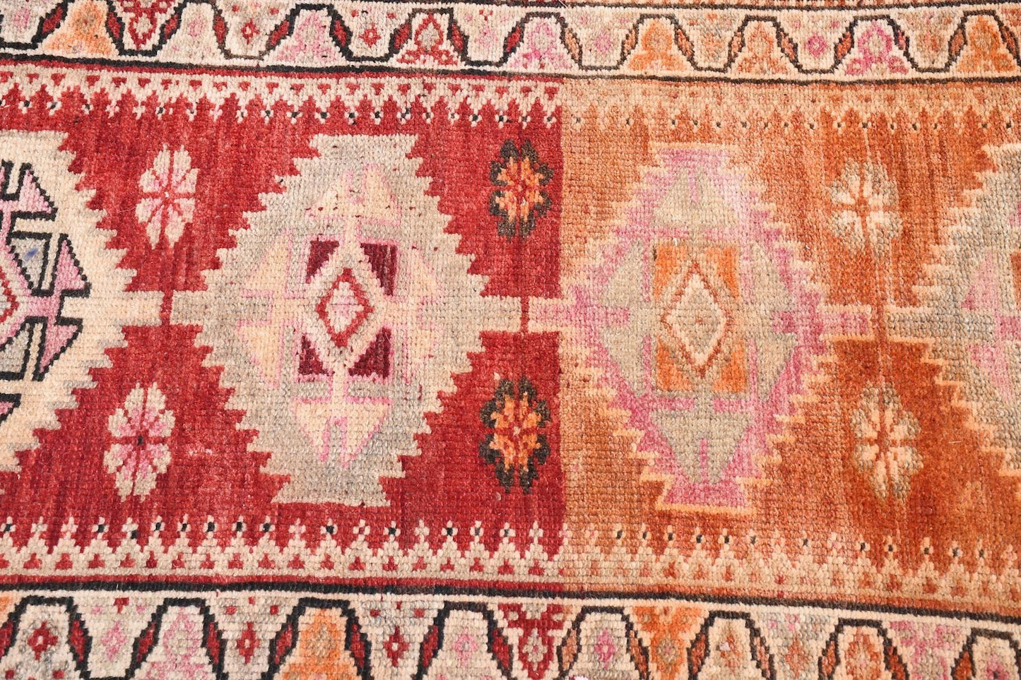 A vintage Kurdish Herki runner featuring tribal geometric motifs in red, orange, and pink tones.