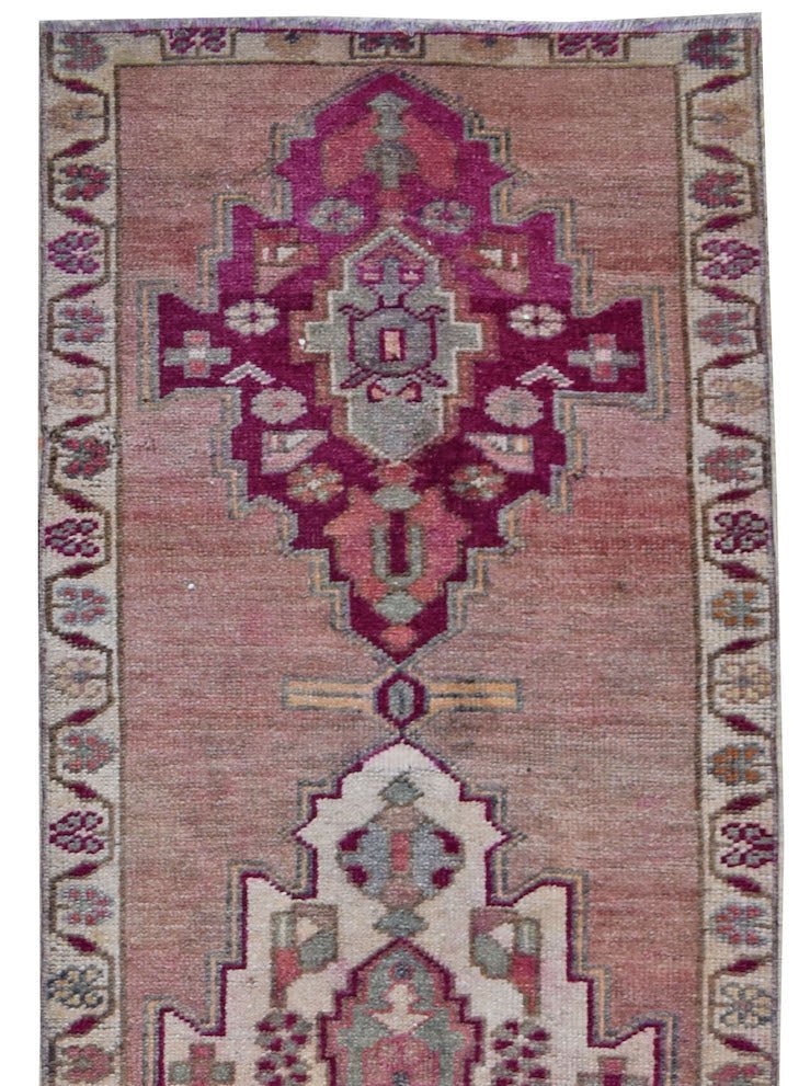 A vintage Kurdish Herki runner featuring tribal motifs in shades of pink, magenta, and grey.