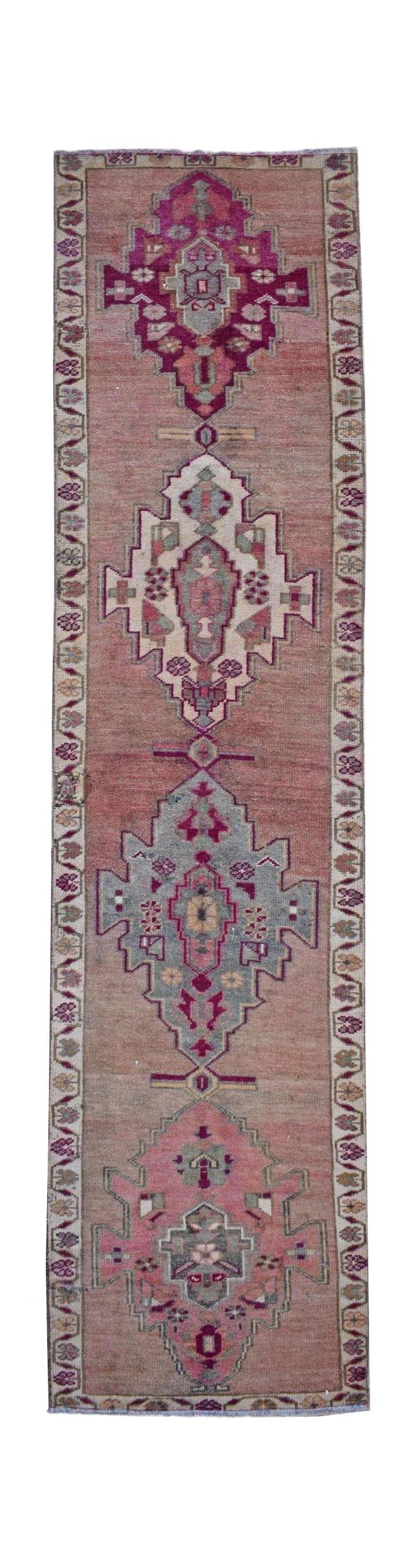 A vintage Kurdish Herki runner featuring geometric tribal motifs in pink and grey tones.