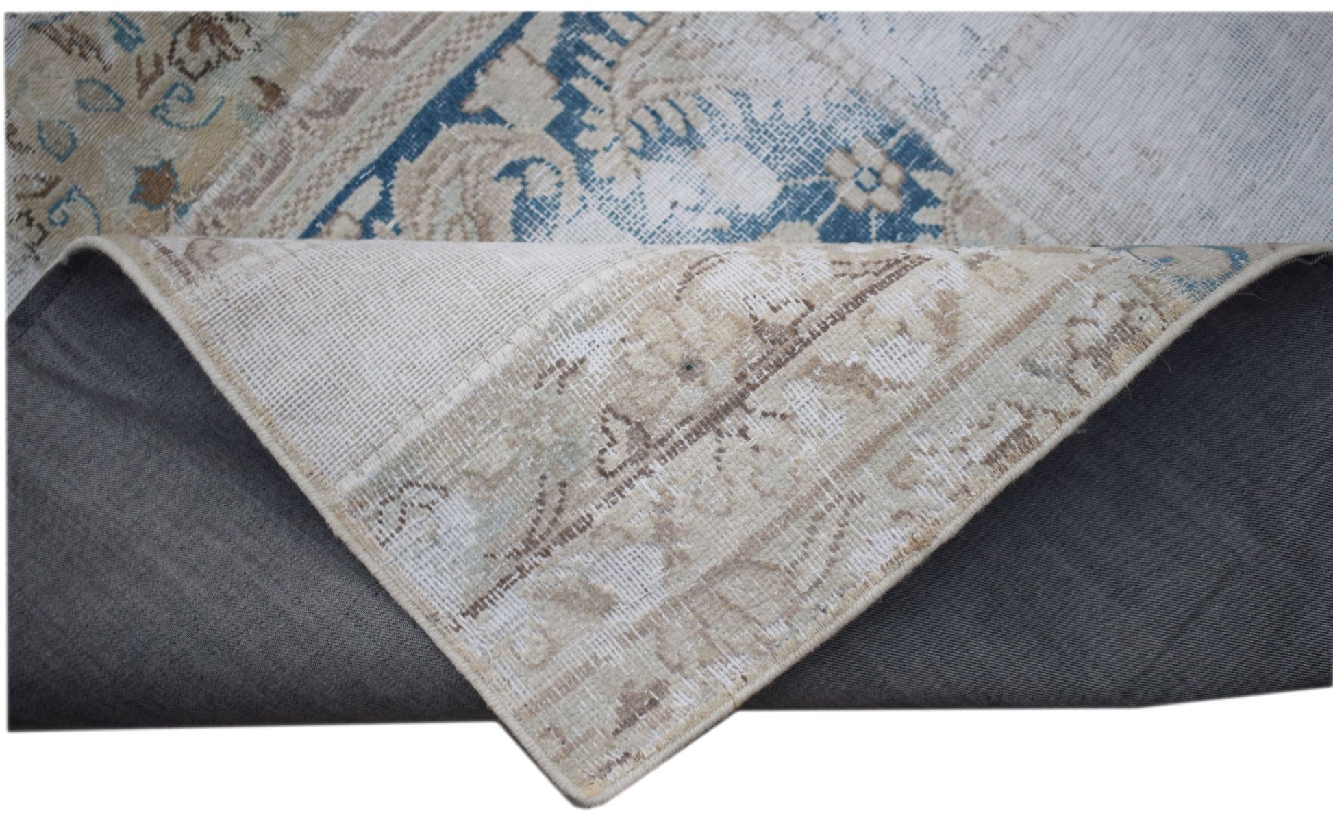 A vintage patchwork rug with blue and beige floral patterns, shown folded to reveal its backing.
