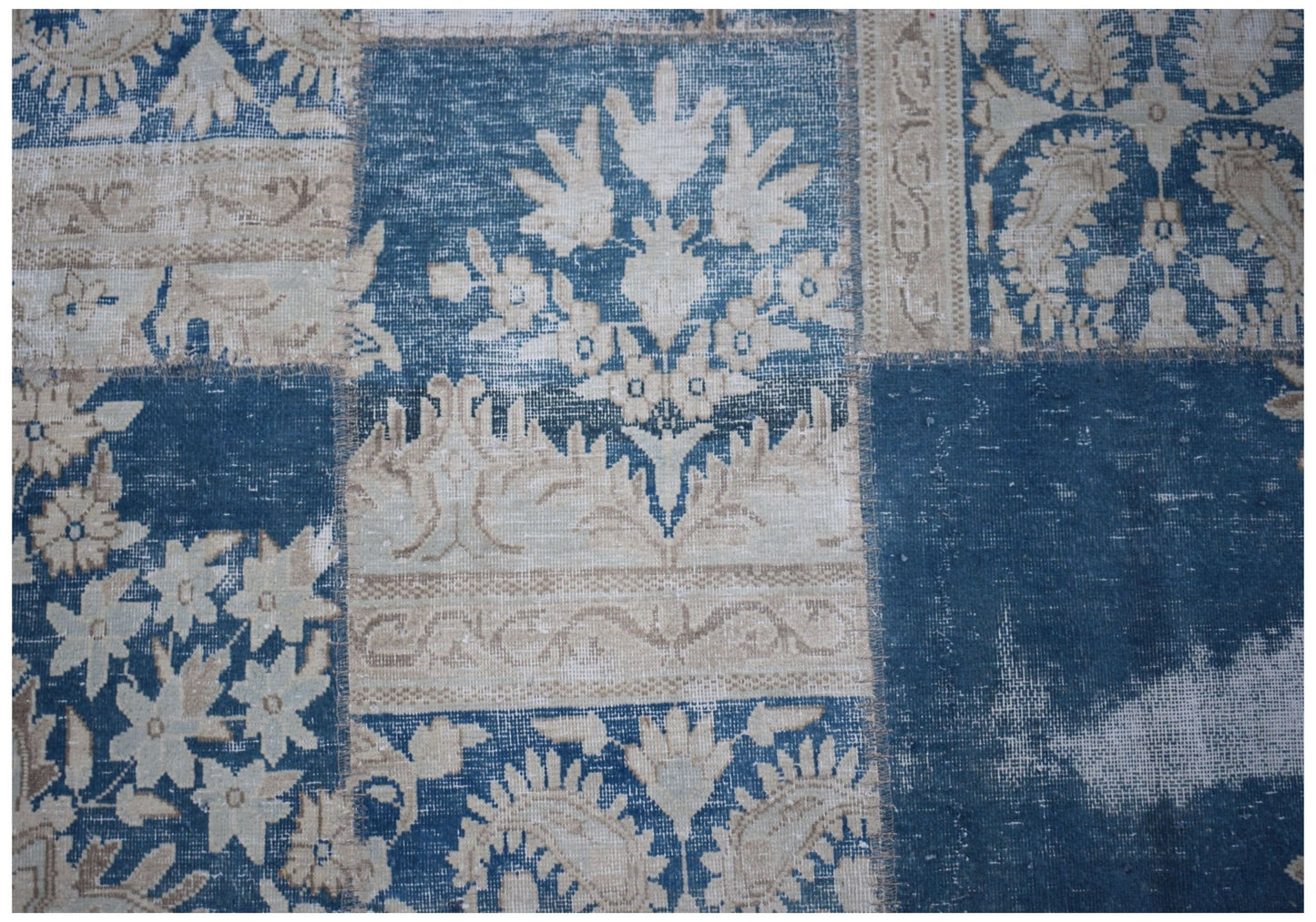A vintage patchwork rug featuring a blue and beige floral pattern with visible stitched seams.