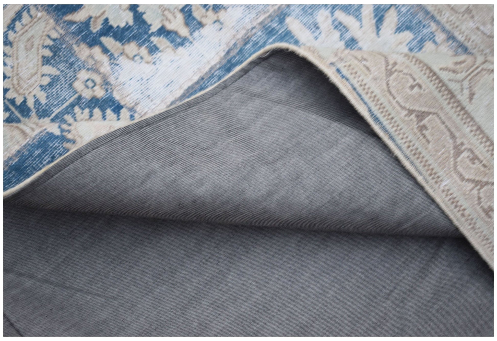 A corner of a vintage patchwork rug is folded back to reveal its grey fabric backing.