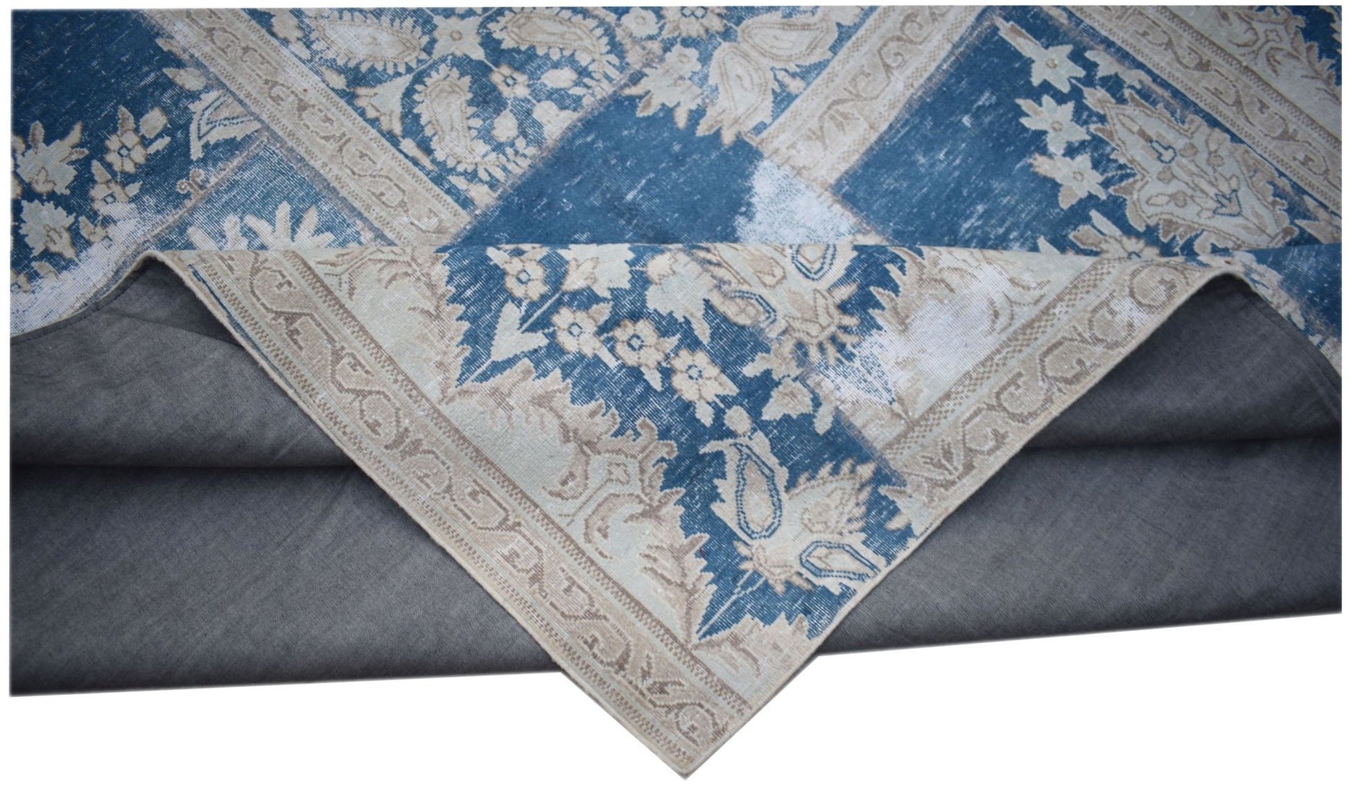 A vintage patchwork rug featuring blue and beige floral patterns with a grey fabric backing.