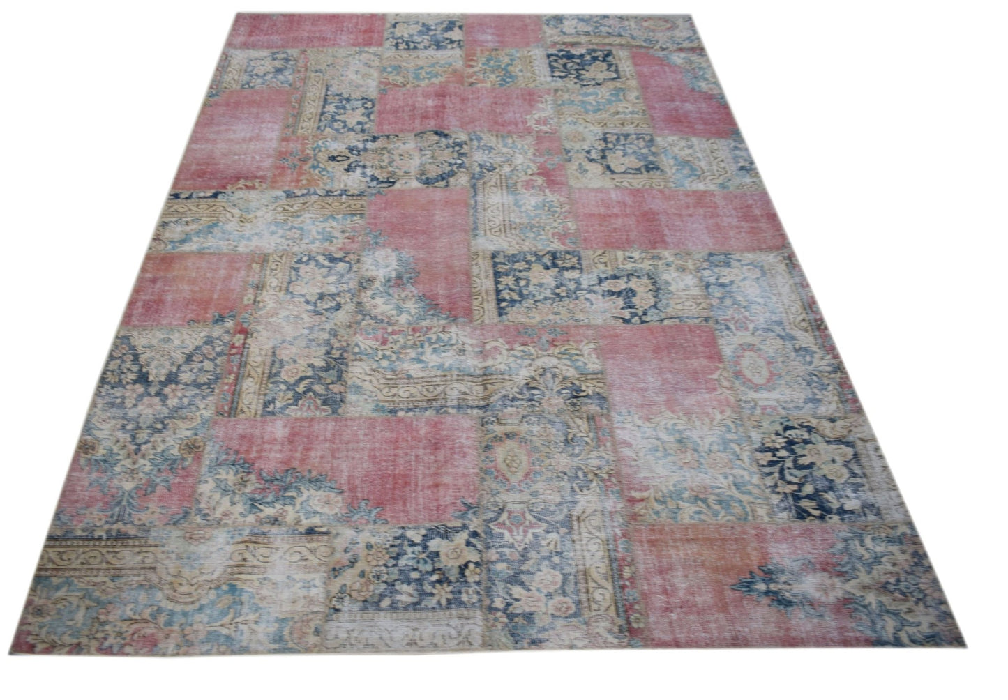 A rectangular vintage patchwork rug featuring a distressed pattern of pink and blue floral motifs.