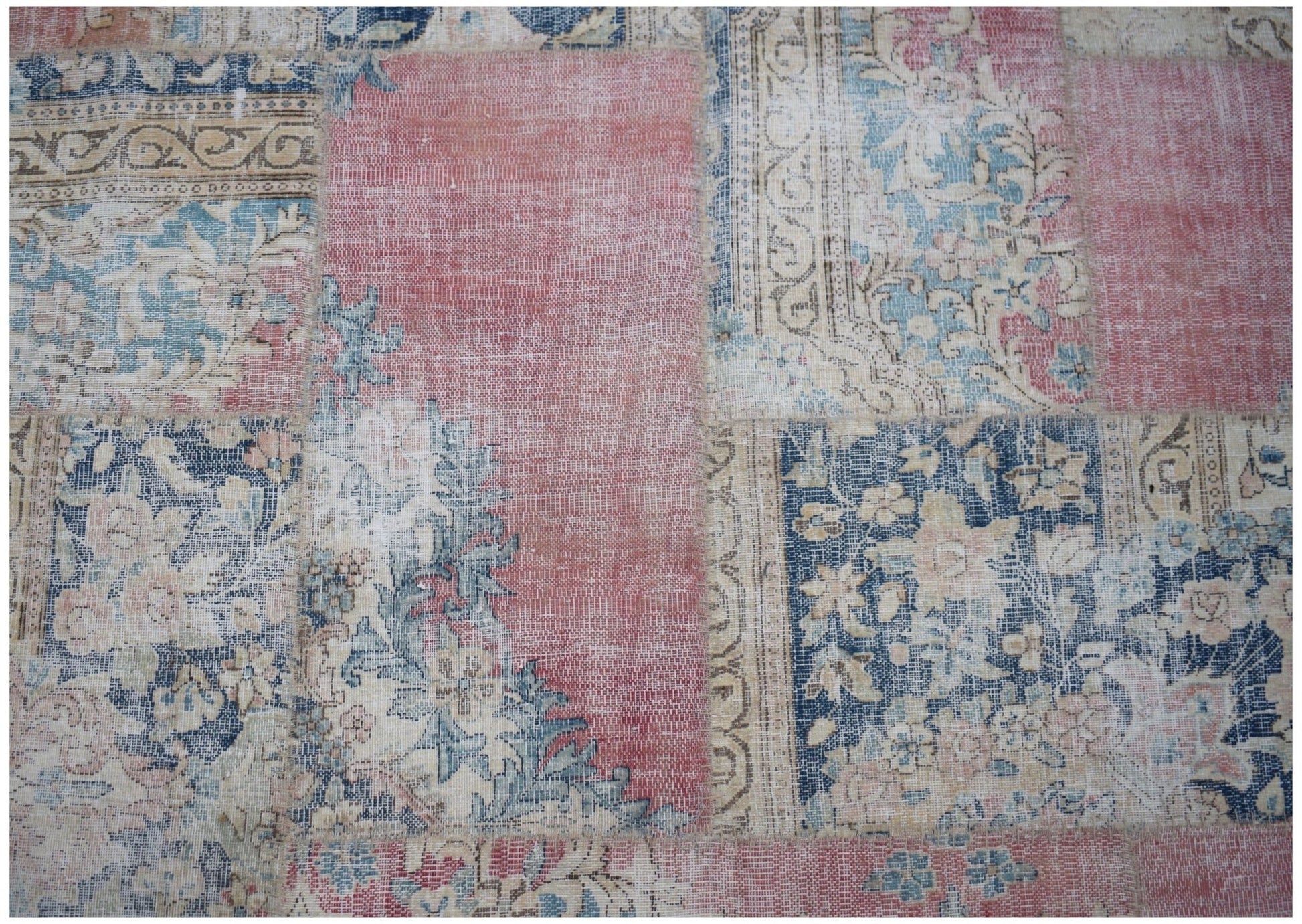 A vintage patchwork rug featuring a mix of floral and geometric patterns in faded pink and blue.