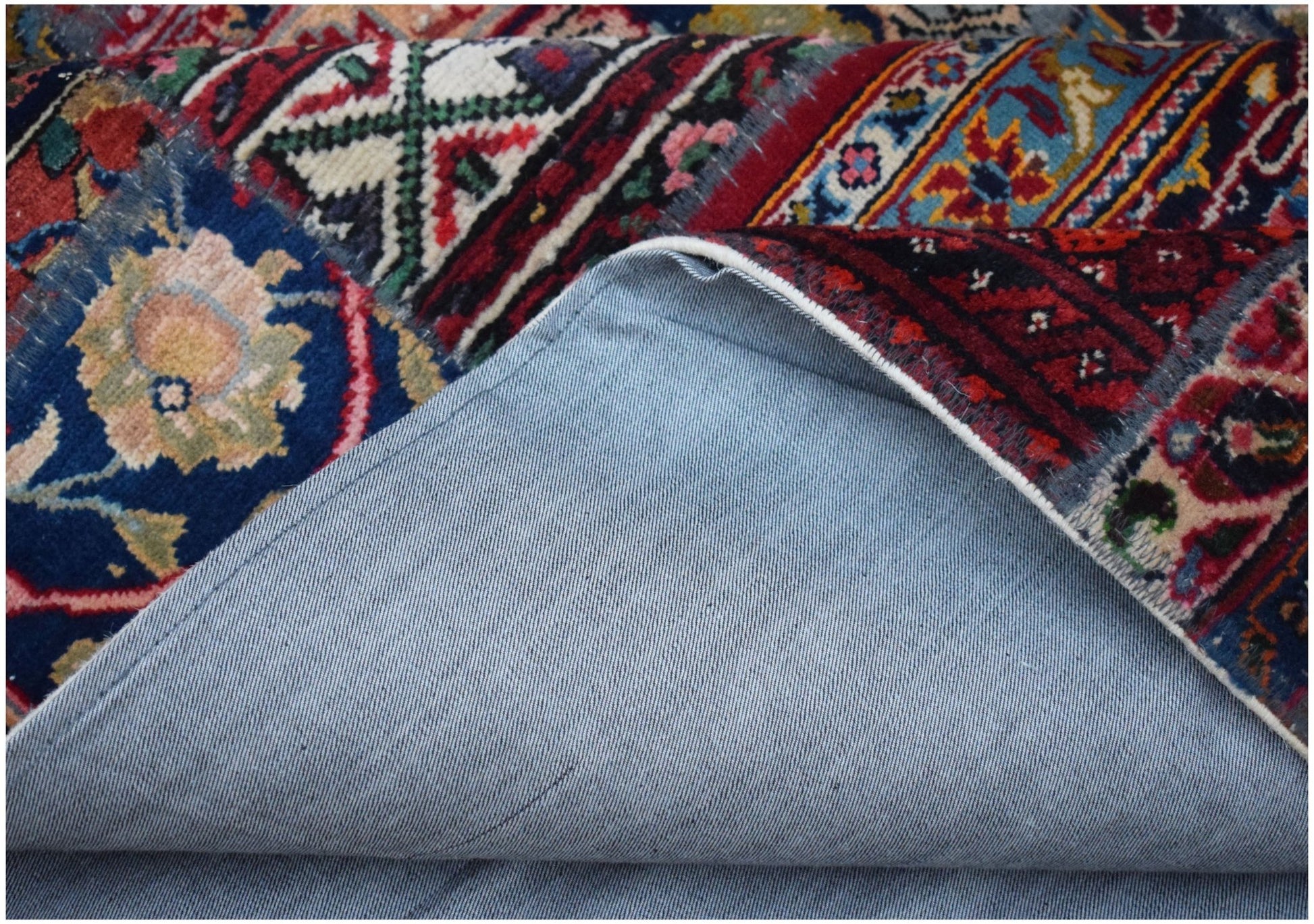 A vintage patchwork rug with a blue denim backing folded to reveal colorful wool patterns.
