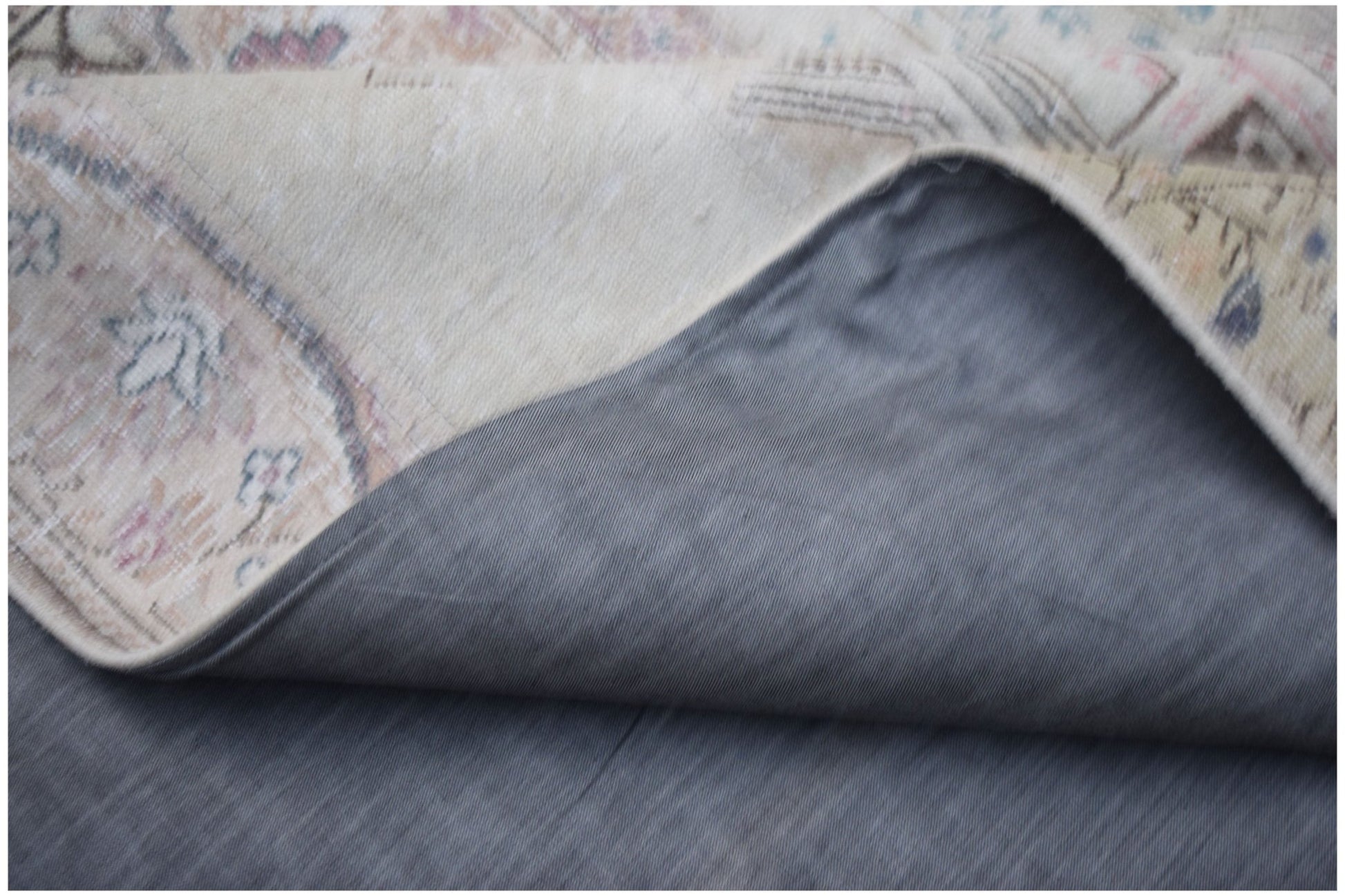A corner of a vintage patchwork rug is folded back to reveal its grey cotton backing.