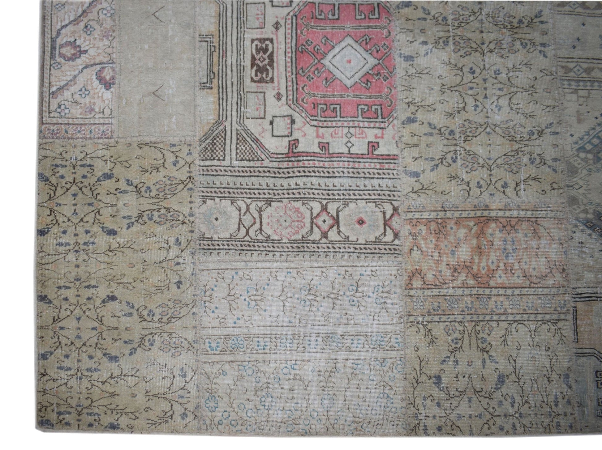 A handmade vintage patchwork rug featuring a mix of faded floral and geometric patterns in wool.