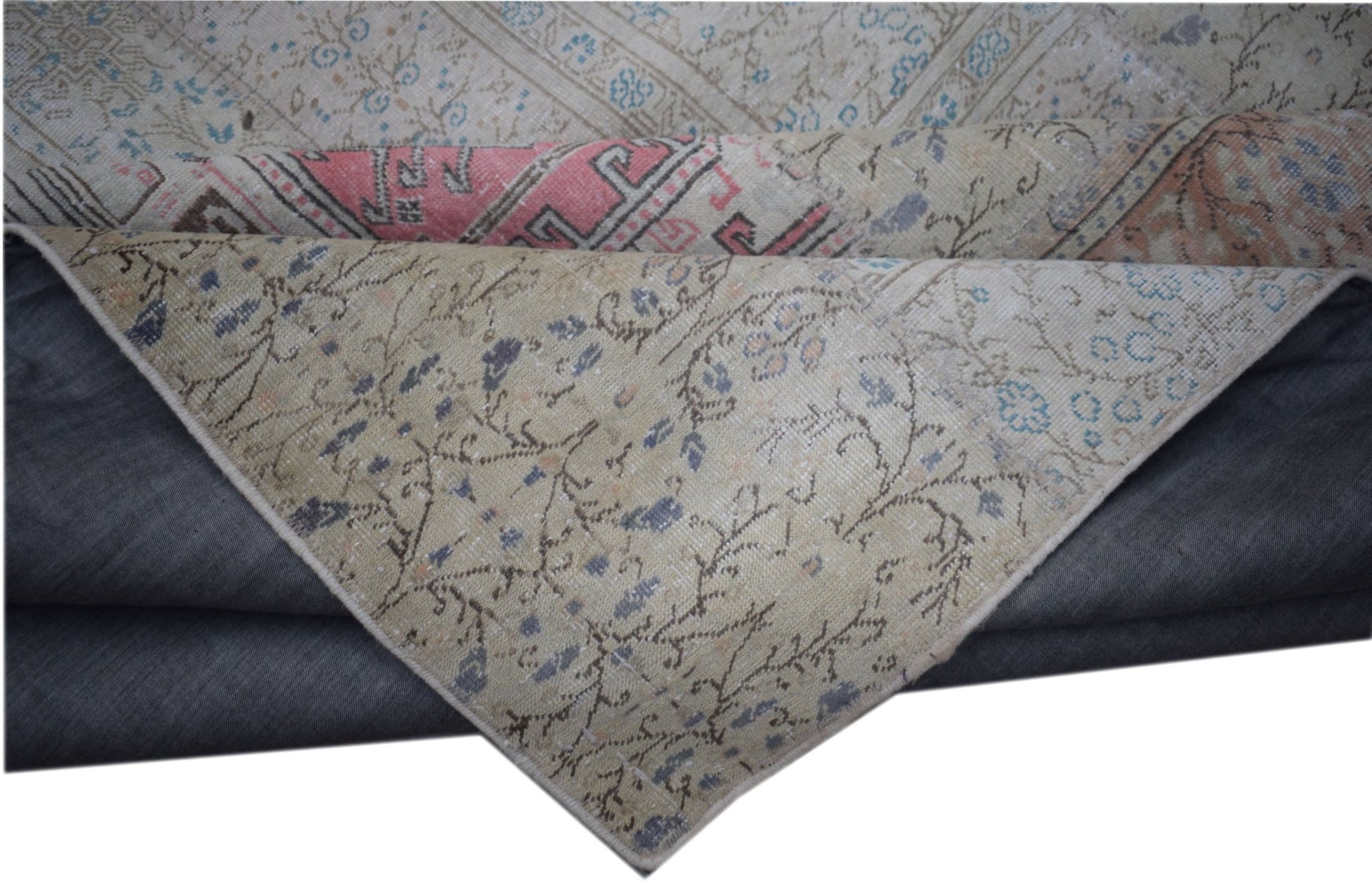 A vintage patchwork rug with a folded corner revealing a floral pattern in muted tones.