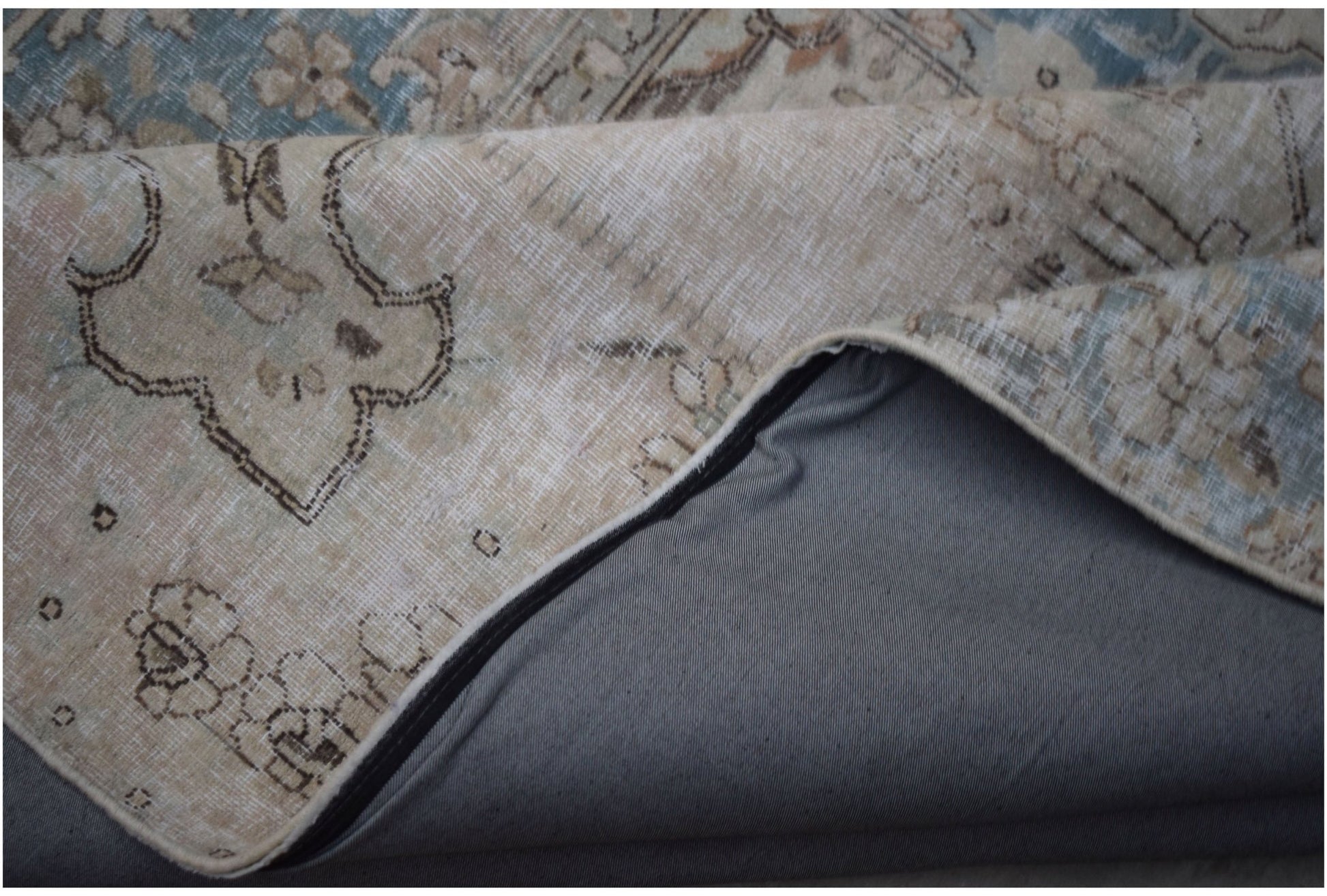 A corner of a vintage patchwork rug with a floral pattern folded to reveal its grey fabric backing.