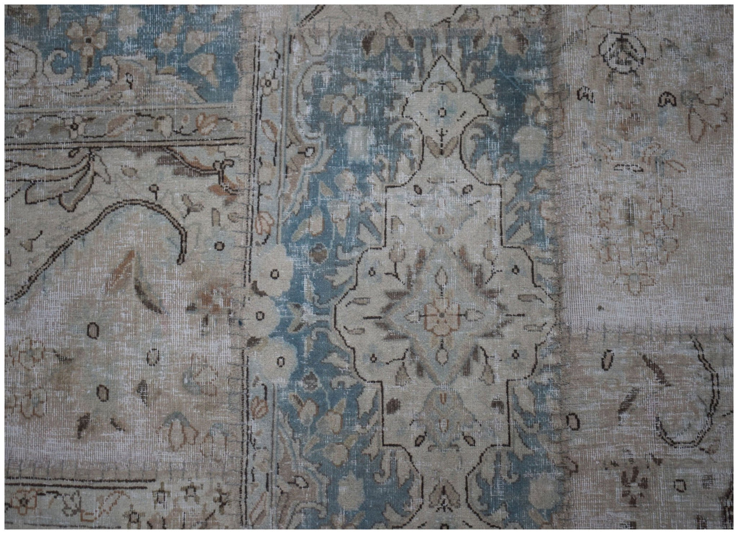 A handmade patchwork rug featuring faded blue and beige floral patterns in a vintage style.