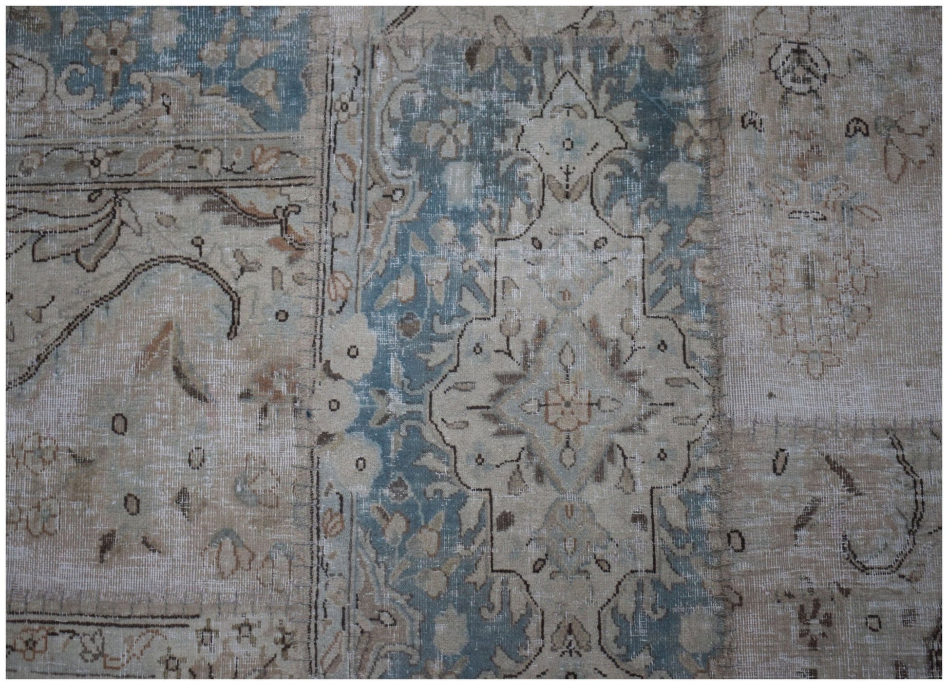 A handmade patchwork rug featuring faded blue and beige floral patterns in a vintage style.