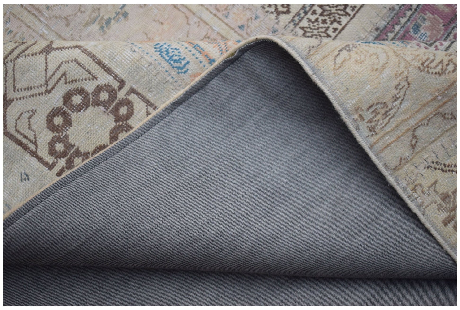 A corner of a handmade vintage patchwork rug showing its patterned wool top and cotton backing.