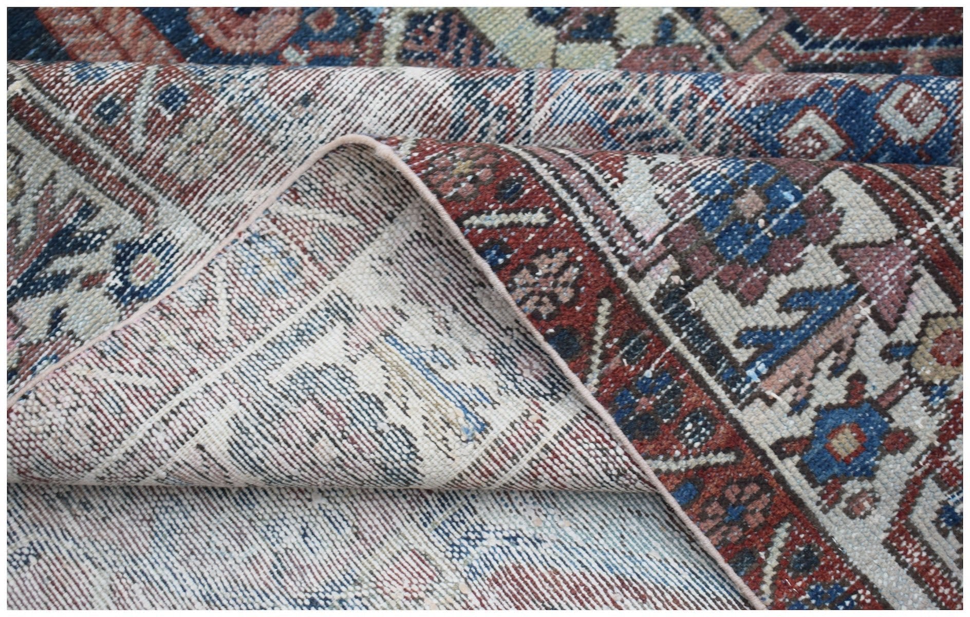 A vintage Persian Bakhtiari rug with a folded corner showing its intricate red and blue pattern.
