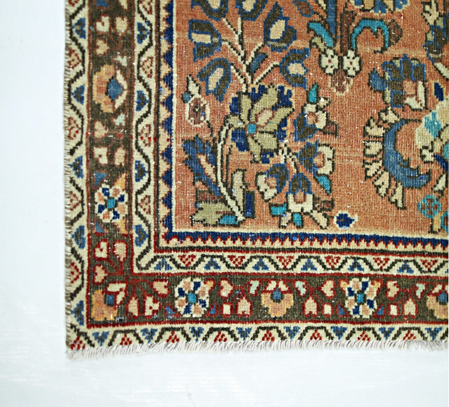 A vintage Persian runner featuring a floral pattern in blue and cream on a terracotta background.