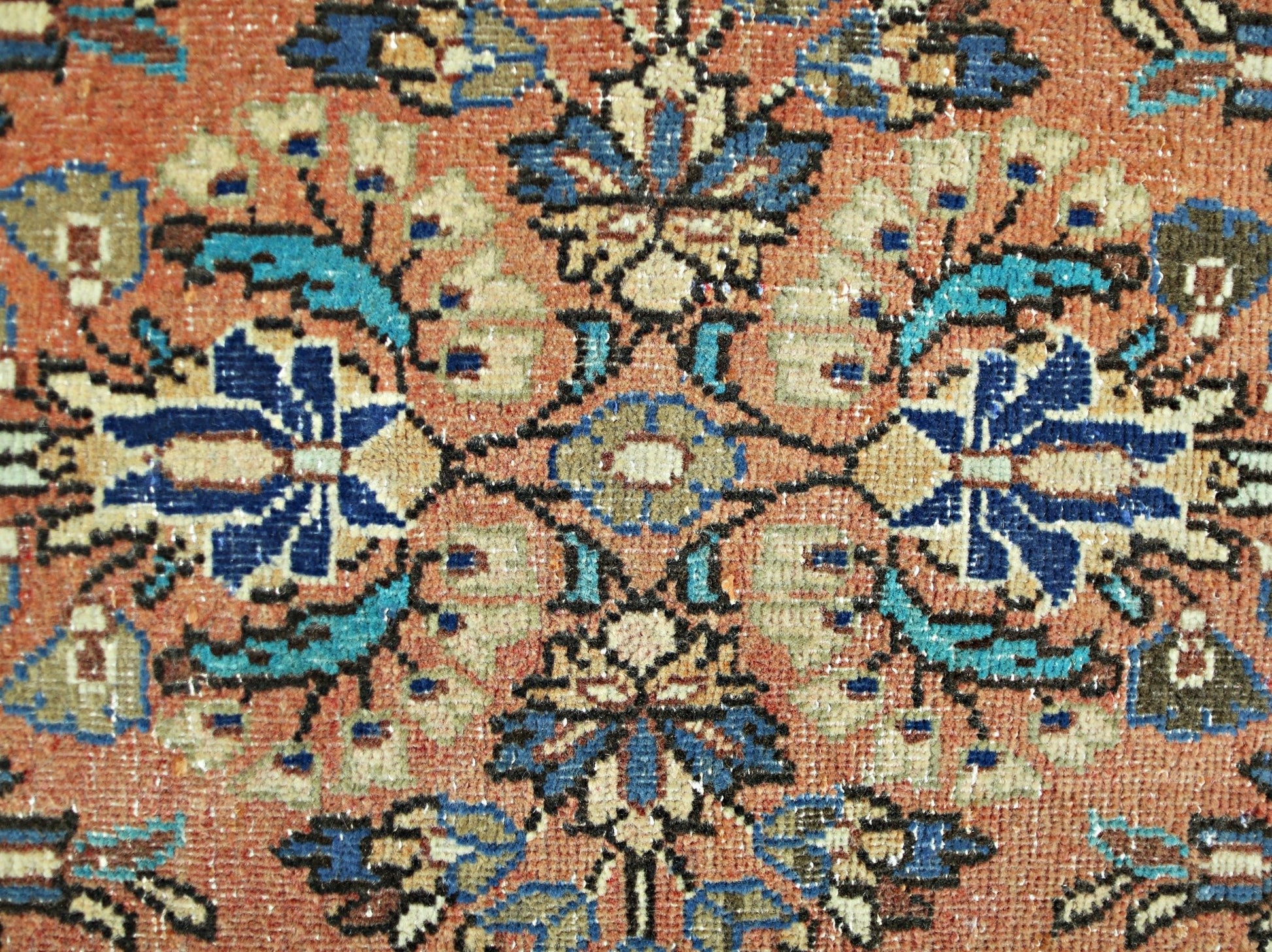 A close-up of a vintage Persian runner featuring a symmetrical floral pattern in blue and tan.