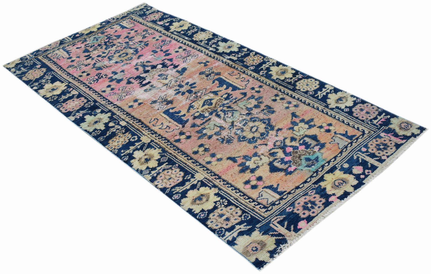 A vintage handwoven Persian runner featuring a faded pink and orange field with a dark blue border.