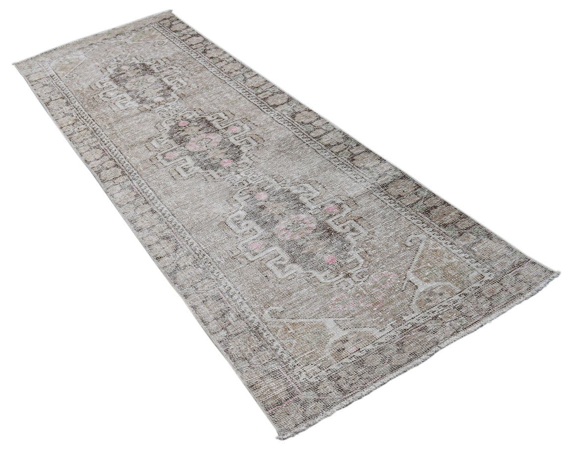 A vintage handwoven Persian runner rug featuring a faded geometric pattern in neutral tones.