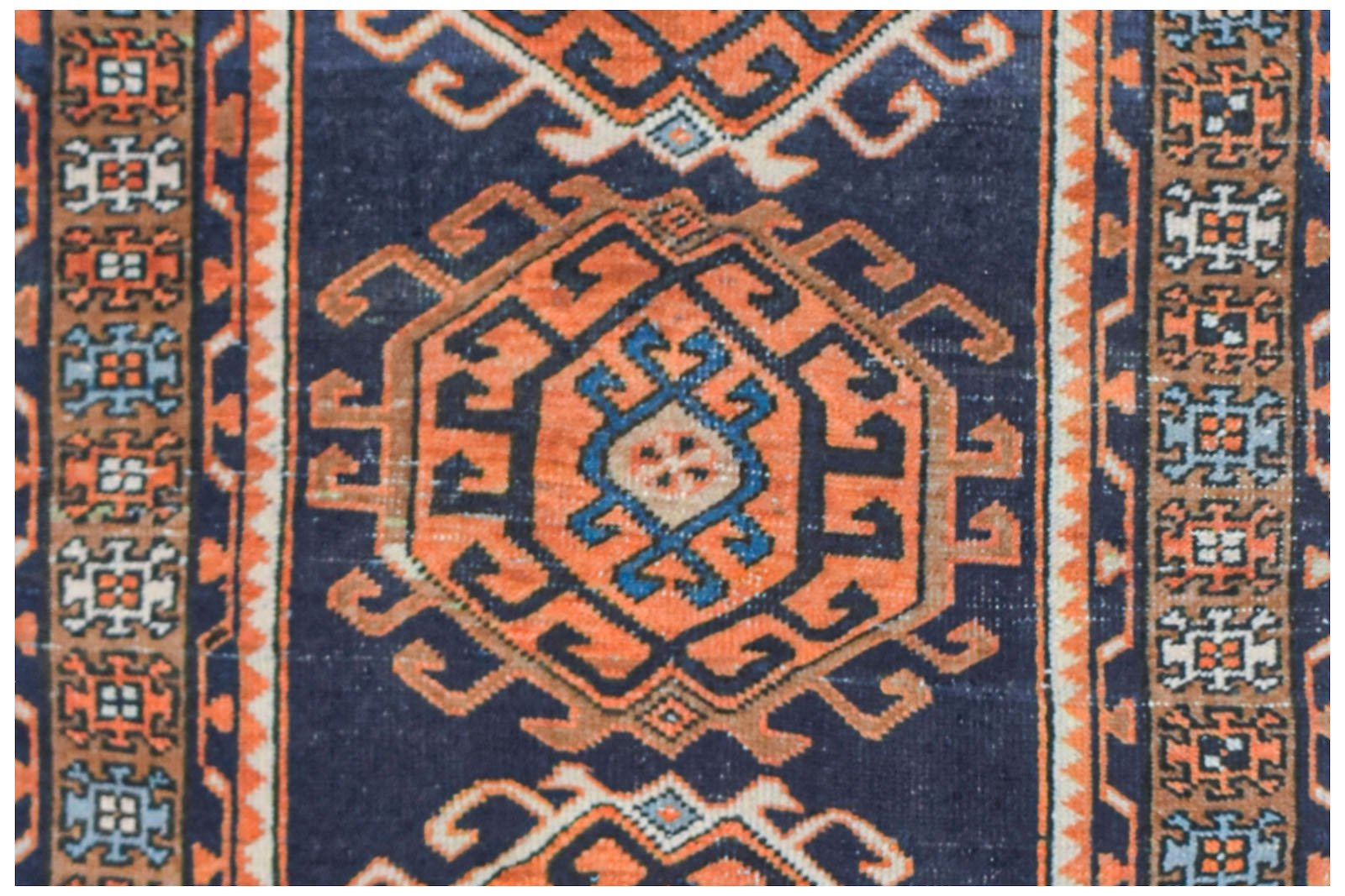A vintage handwoven Persian runner featuring geometric orange medallions on a dark blue background.