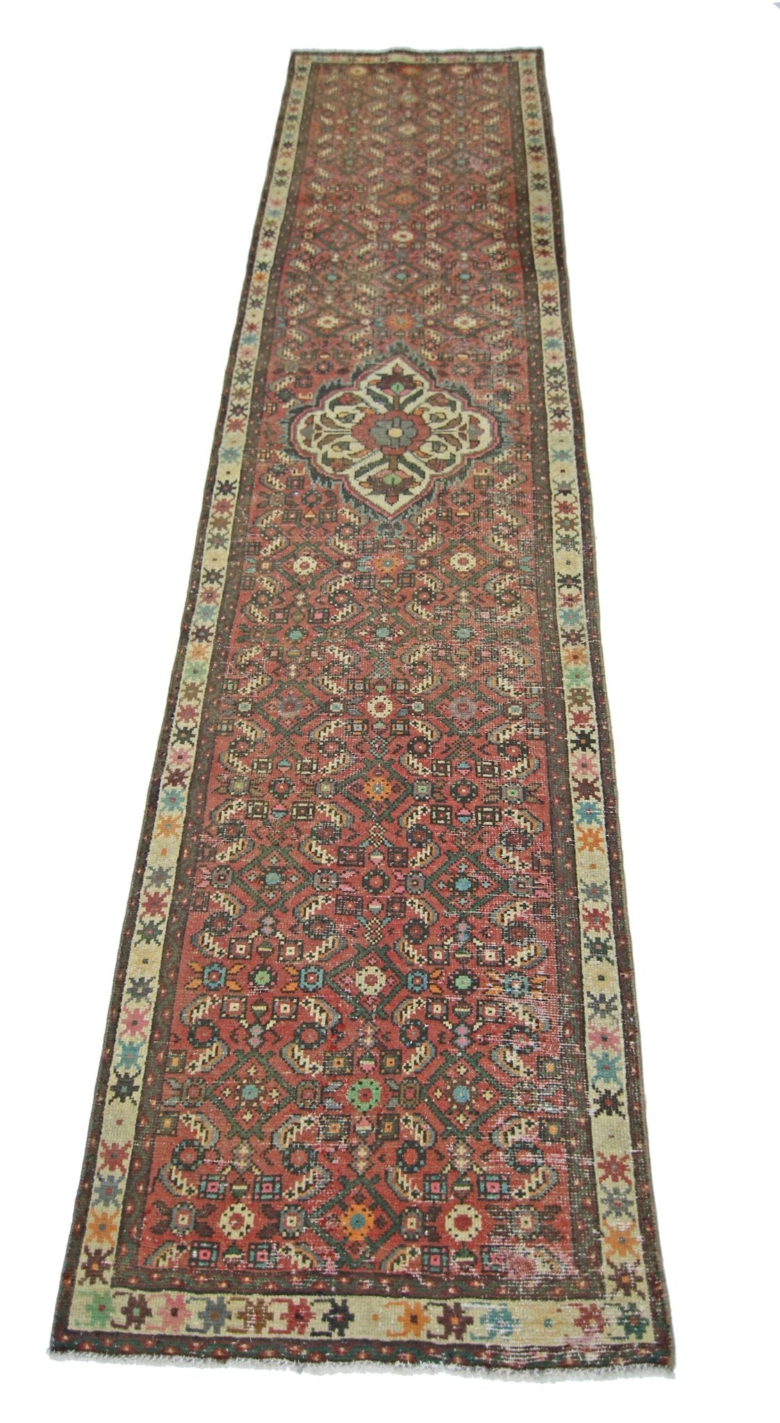 A long, handmade vintage Persian runner rug featuring a geometric floral pattern in red and cream.