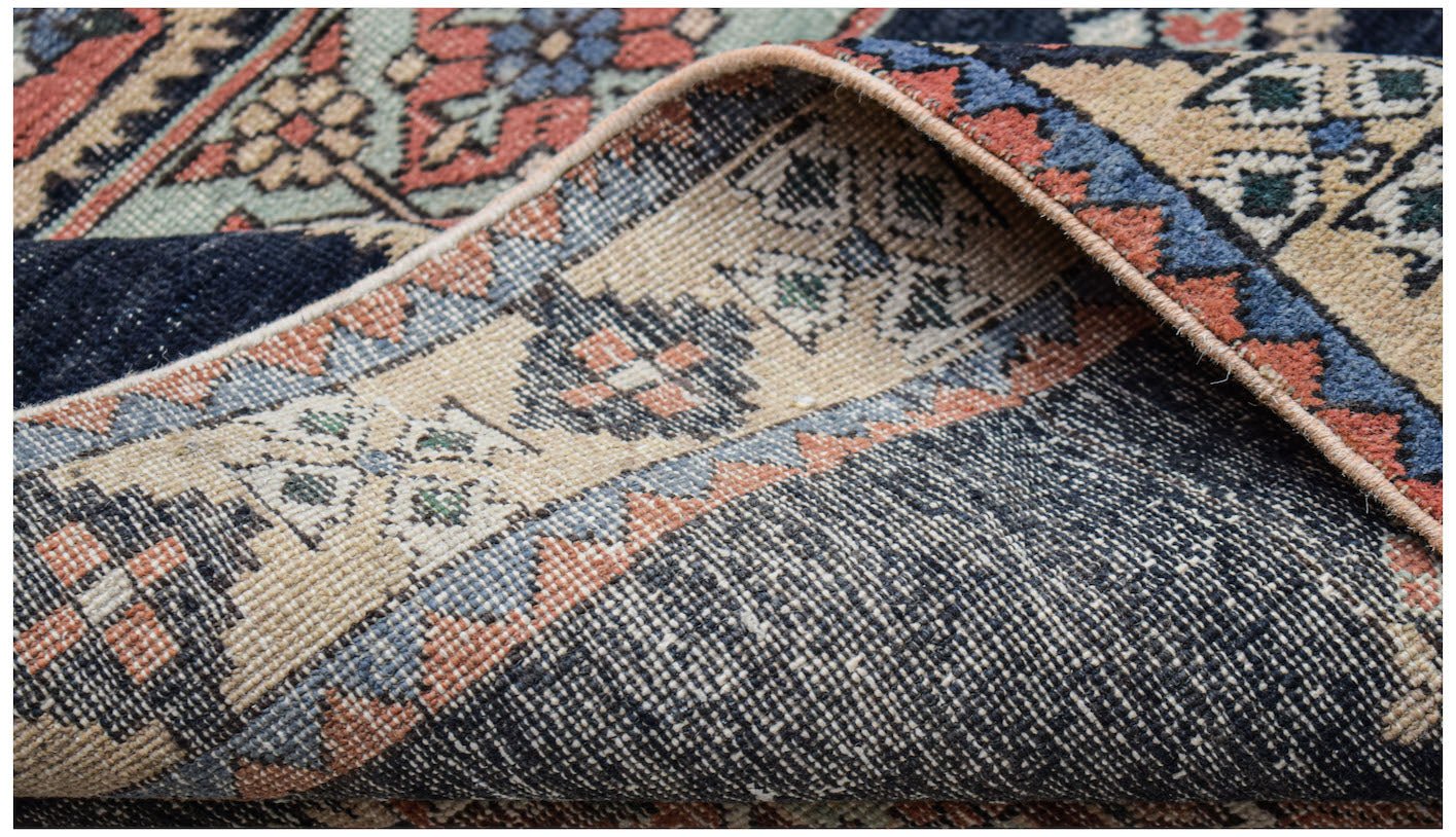 A folded vintage Persian Ardabil runner featuring a dark blue field and intricate floral patterns.