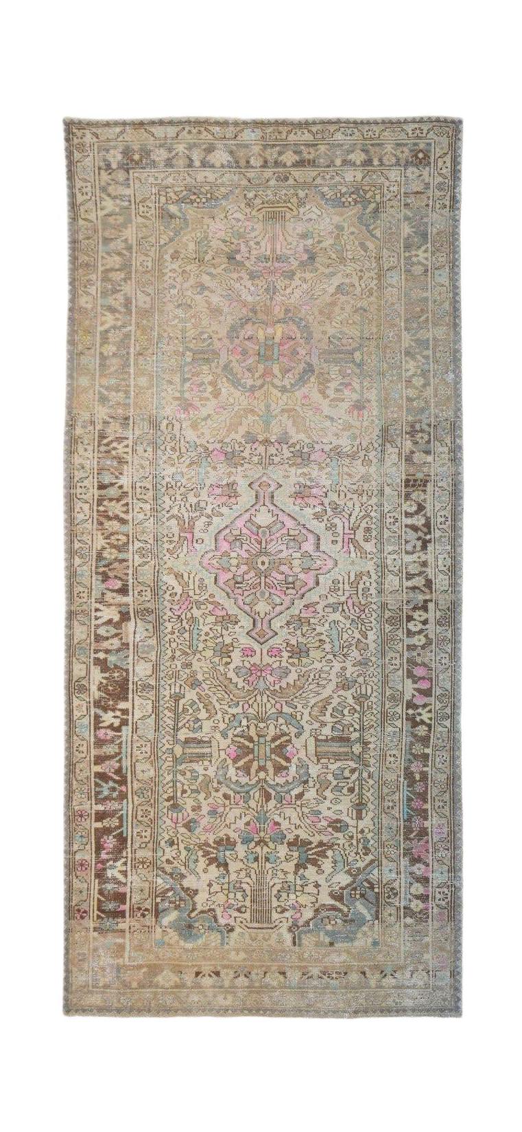 A handwoven vintage Persian runner featuring a faded floral pattern in pink, blue, and beige tones.