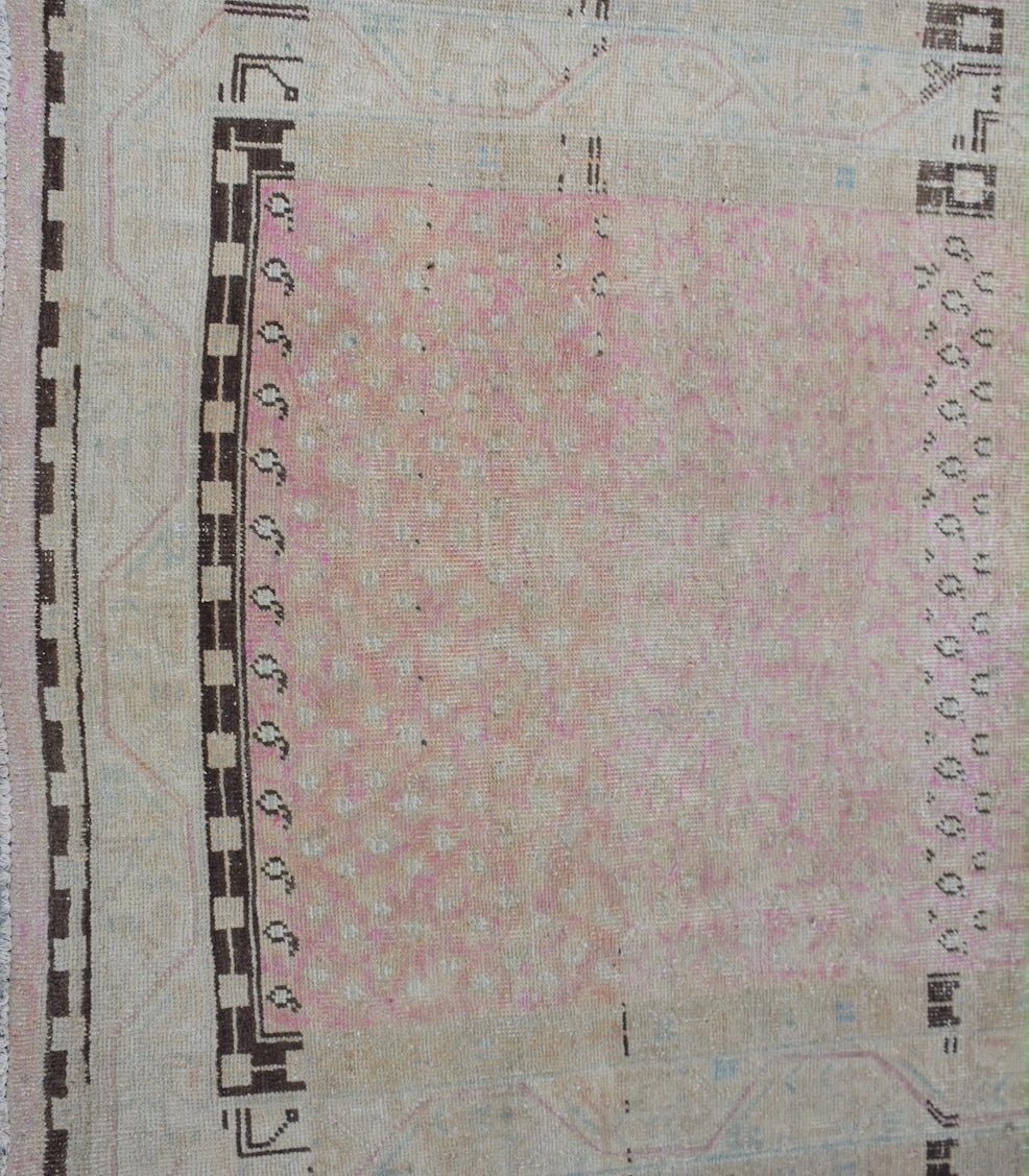A vintage Persian runner featuring a faded pink central field with geometric borders.