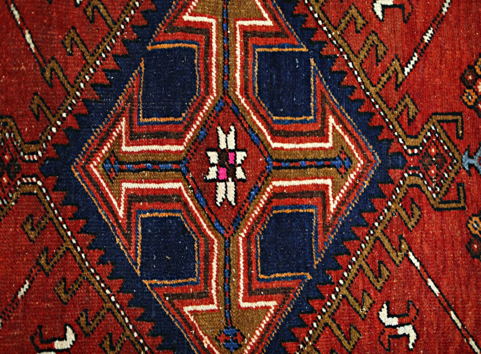 A vintage Persian runner featuring a geometric diamond medallion in red, blue, and brown wool.